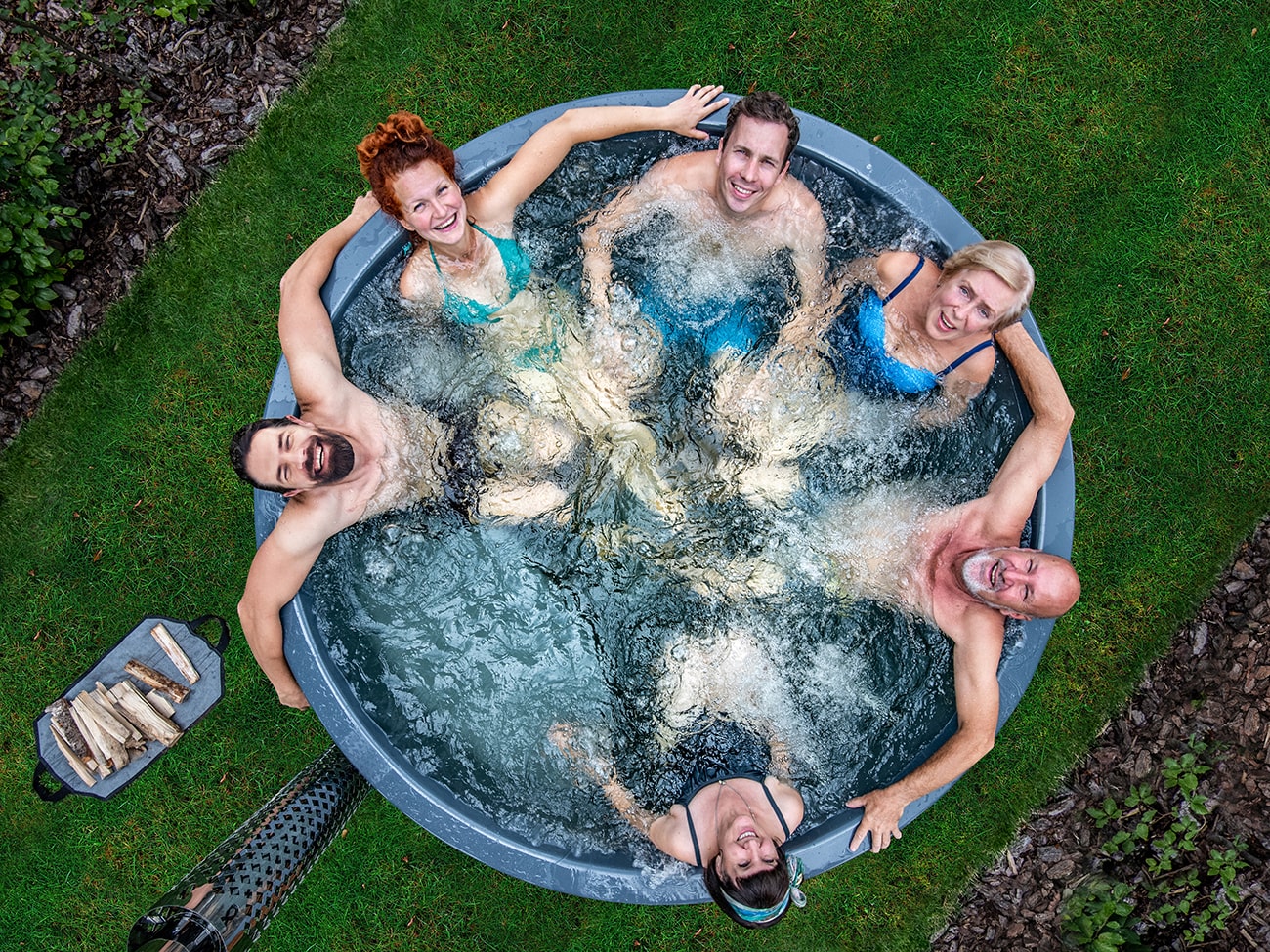 Overhead view of six adults smiling and relaxing in a round hot tub with bubbling water.