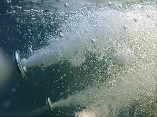 Close-up underwater view of two hot tub jets releasing streams of aerated, bubbling water.