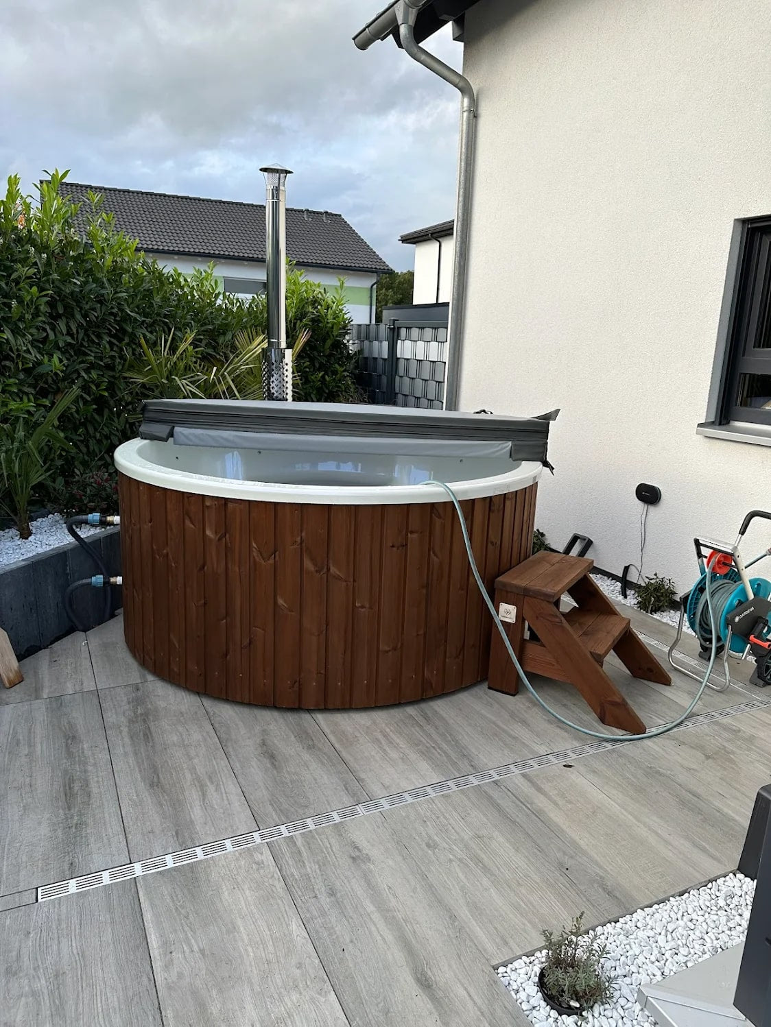 Gardenvity wood fired hot tub installed on a tiled terrace beside a modern house.