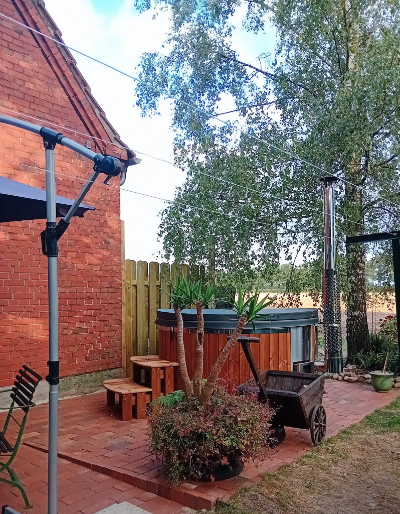 Gardenvity wood fired hot tub in small backyard with red brick walls and garden plants.