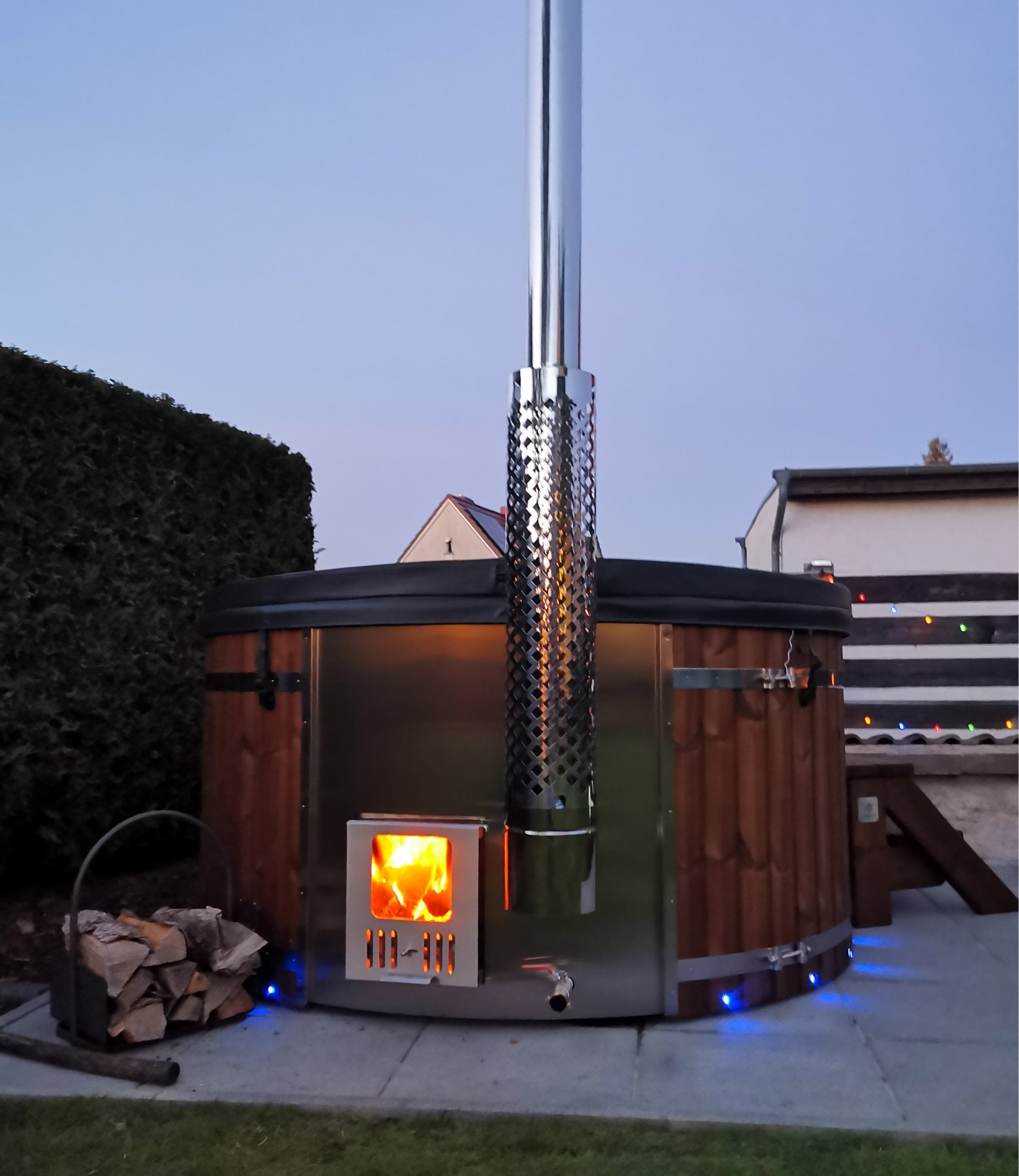 Gardenvity wood fired hot tub with fire burning inside stove in cozy backyard setting.