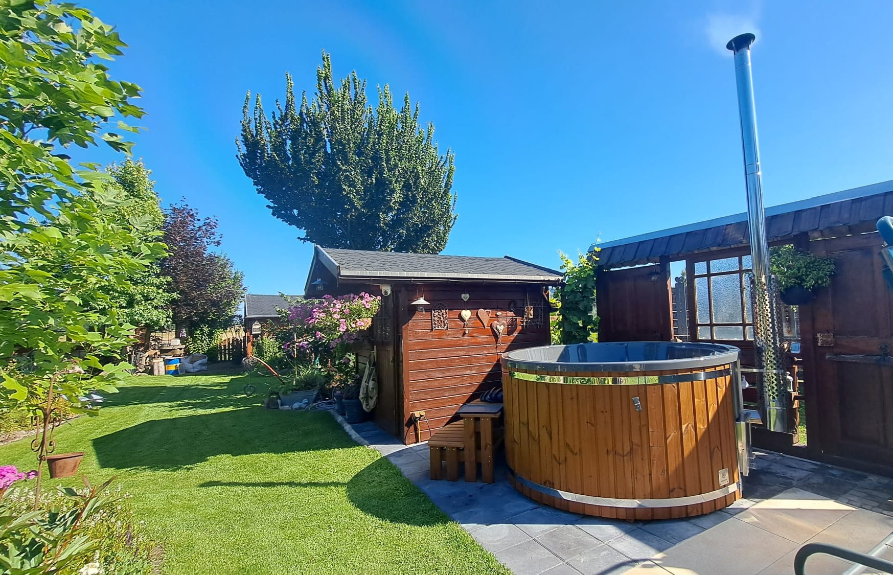 Gardenvity wood fired hot tub in modern garden with wooden shed and manicured lawn.