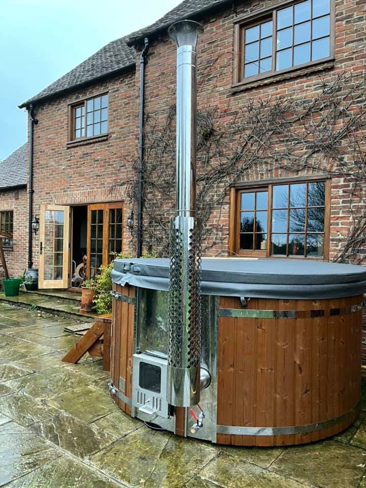 Gardenvity wood fired hot tub on stone patio beside traditional brick house in the UK