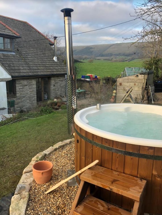 Gardenvity wood fired hot tub beside old stone farmhouse with scenic countryside view.