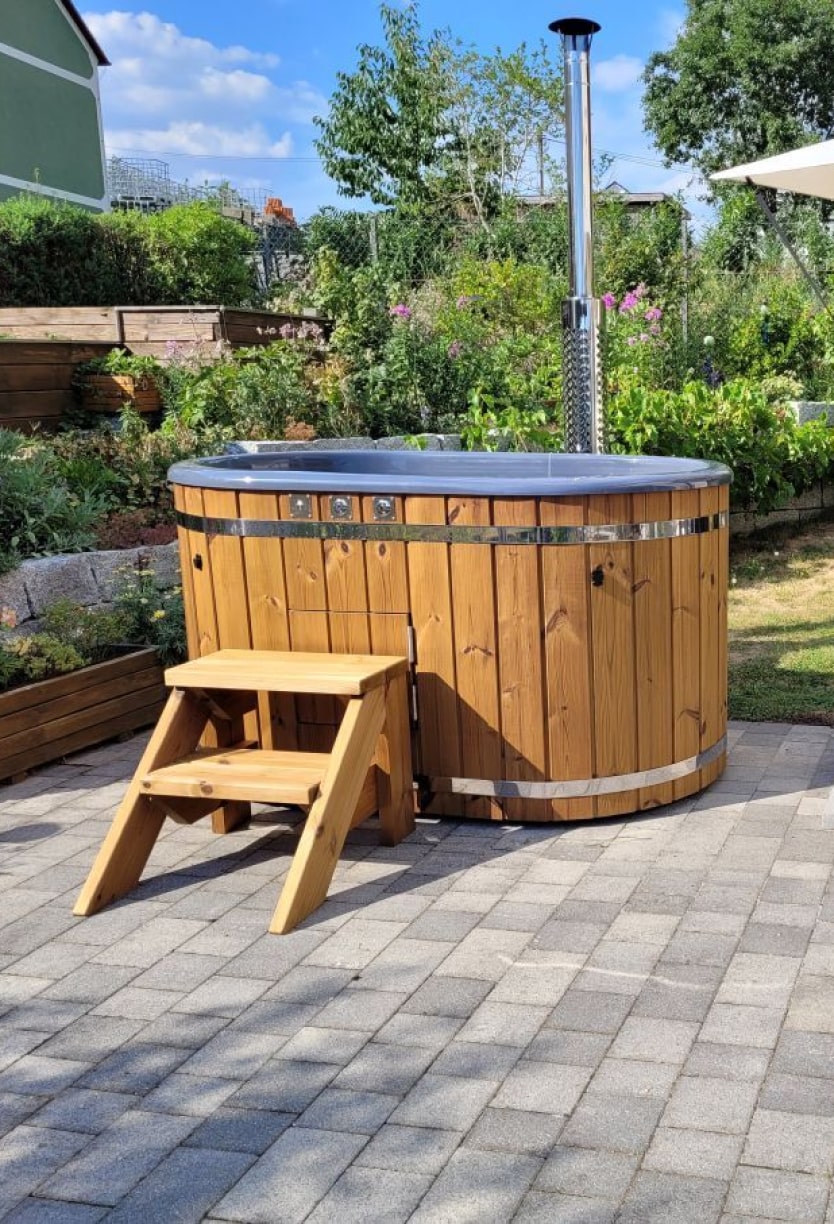 Gardenvity wood fired hot tub on tiled patio in German garden with wooden standard steps.