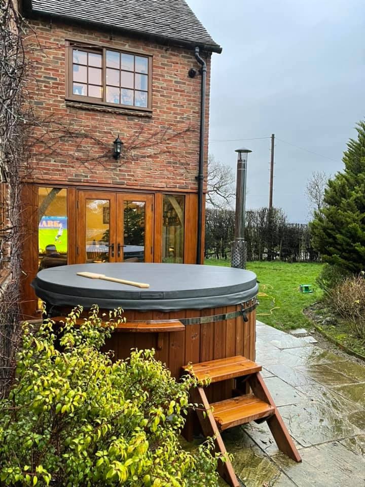 Gardenvity wood fired hot tub installed in front of brick house with lawn and countryside view.