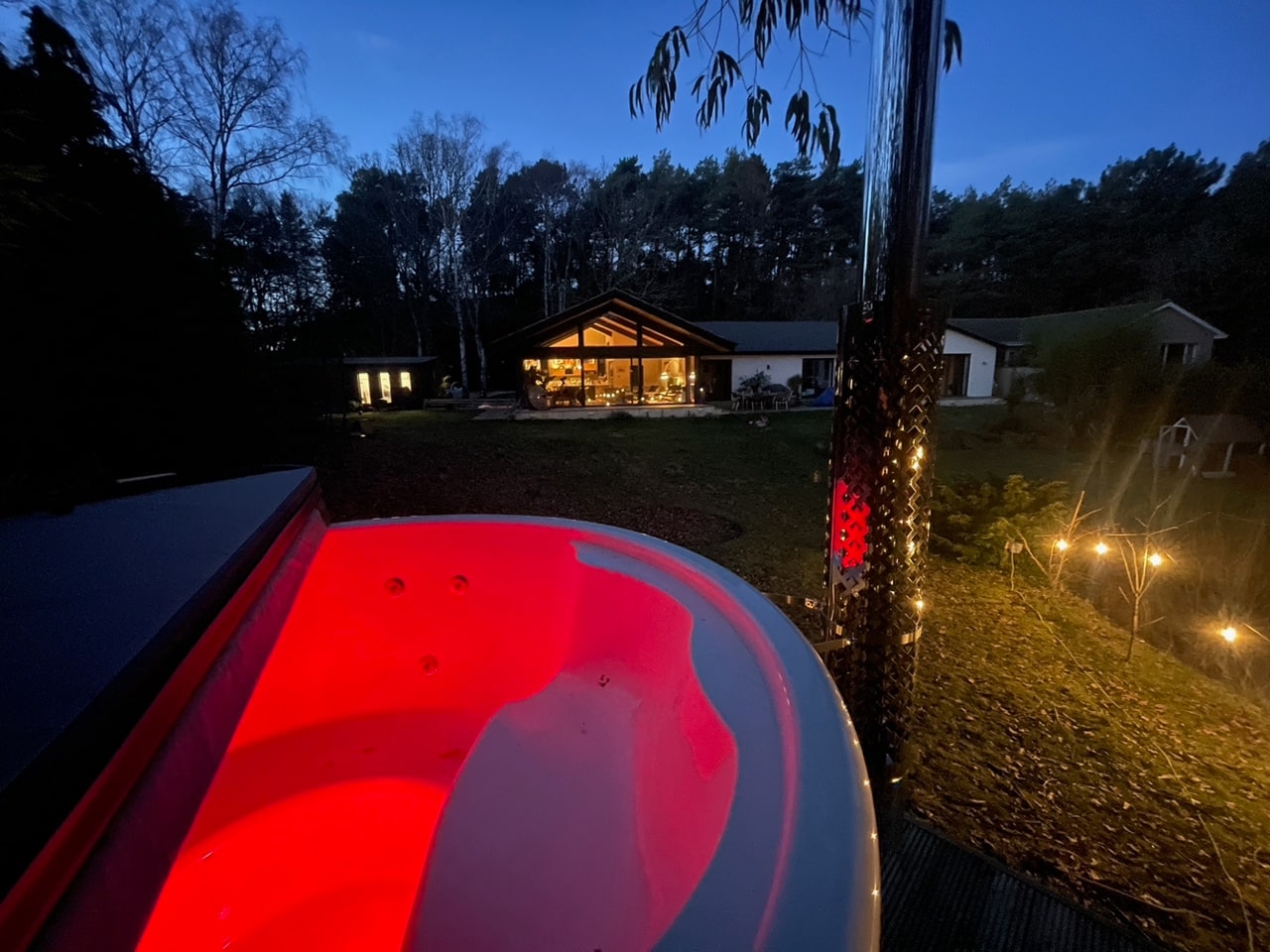Gardenvity wood fired hot tub with red underwater lighting in dark garden evening.