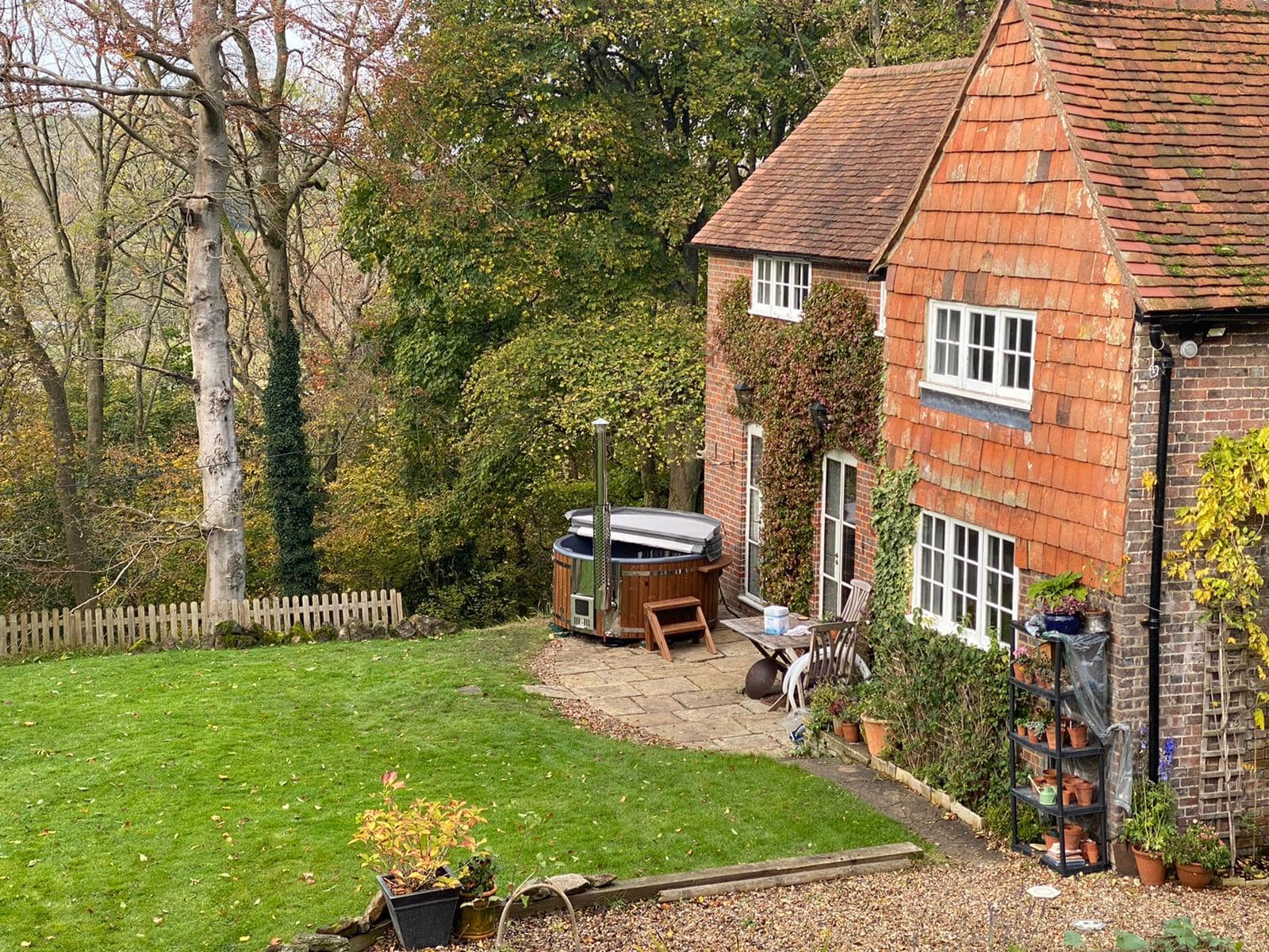 Gardenvity wood fired hot tub beside a red brick countryside house with rustic charm.