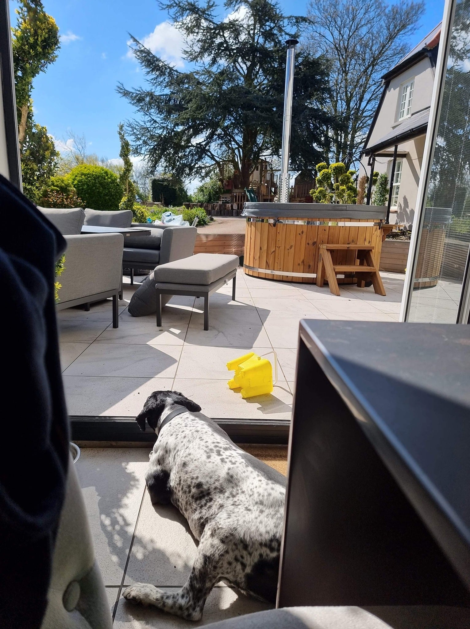 Gardenvity wood fired hot tub on a modern patio with outdoor furniture and dog in view